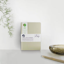 Load image into Gallery viewer, Notebook with a white label on a light surface with a plant and candle in the background