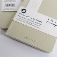 Load image into Gallery viewer, A close-up of a Sugseed notebook with a white paper band label around it, photographed on a clean white background. The notebook cover is a pale warm beige/gray tone, and the label includes the Sugseed name and a leaf logo.