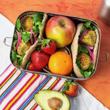 Load image into Gallery viewer, Metal lunch box with falafel sandwiches, fruits, and an avocado on a colorful striped towel.