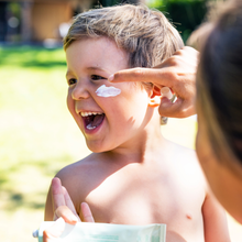 Load image into Gallery viewer, Smiling child outside in the garden, having suncream applied to his face