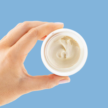 Load image into Gallery viewer, Hand holding a jar of cream against a blue background