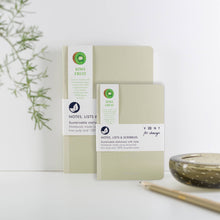 Load image into Gallery viewer, Two Kiwi Fruit brand notebooks in a soft sage green color, displayed on a white surface with a decorative bowl and pencil in the background.