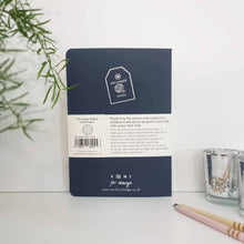 Load image into Gallery viewer, Navy blue notebook with white label on a white surface with a plant and pencil in the background
