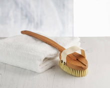 Load image into Gallery viewer, A wooden bath brush with a long handle and natural bristles, resting on a white towel with a part of the towel wrapped around the handle.