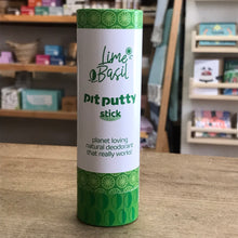 Load image into Gallery viewer, Cylindrical container of 'Lime Basil Pit Putty Stick' natural deodorant on a wooden surface with shelves in the background.