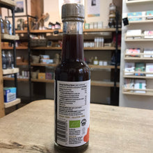Load image into Gallery viewer, Bottle of dark liquid with a label on a wooden surface in a store setting