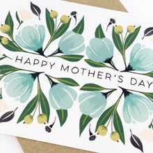 Load image into Gallery viewer, A floral Mother's Day card with the text 'Happy Mother's Day' surrounded by a design of soft pinks and lush greens, depicting flowers and leaves. The card is placed on a brown surface.