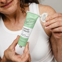 Load image into Gallery viewer, Woman holding a tube of UpCircle hand cream with visible branding.