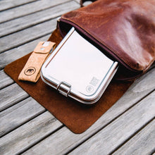 Load image into Gallery viewer, Brown leather bag with a metal container on a wooden surface