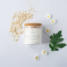 Load image into Gallery viewer, A glass jar with a cork lid labeled 'SKIN SAINT' containing a dry powder mix alongside scattered oats, chamomile flowers, and a leaf on a white background.