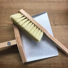 Load image into Gallery viewer, A beige dustpan and brush set made of wood and bristles, displayed on a wooden surface.