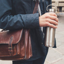Load image into Gallery viewer, Person holding a brown leather satchel and a silver water bottle outdoors.
