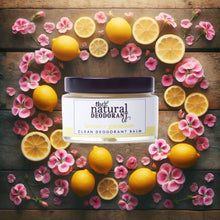 Load image into Gallery viewer, Jar of 'The Natural Deodorant Co.' balm surrounded by lemons and pink flowers on a wooden surface
