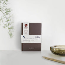 Load image into Gallery viewer, Brown notebook with white label on a light surface with a plant and candle in the background
