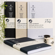 Load image into Gallery viewer, Three VENT for change lined notebooks from RECLAIM are displayed in a styled flat-lay setting. The notebooks come in three colorways: black wool, beige wool, and a light blue-gray cotton blend.
