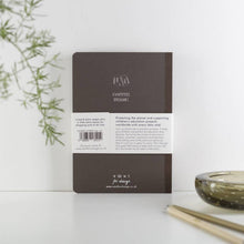 Load image into Gallery viewer, Brown notebook with branding and text on a white surface with greenery
