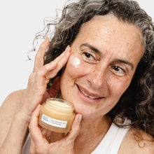 Load image into Gallery viewer, Woman applying cream to her face with a jar of cream in her hand.
