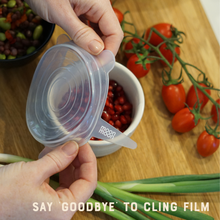 Load image into Gallery viewer, Person using a silicone food cover on a container with tomatoes and green onions on a wooden surface.
