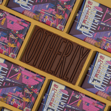 Load image into Gallery viewer, Chocolate bar with 'Otherly' branding surrounded by colorful packaging
