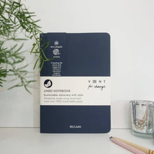 Load image into Gallery viewer, Navy blue notebook with 'Reclaimed Wool' label on a white surface with a plant and glass in the background.

