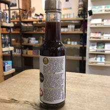 Load image into Gallery viewer, Bottle of syrup with a label on a wooden surface in a store setting
