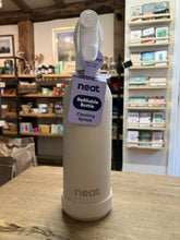 Load image into Gallery viewer, A Neat refillable cleaning spray bottle in a warm off-white color, sitting on a wooden table inside a shop. The bottle has a white spray top and a purple hangtag that reads 'neat Refillable Bottle Cleaning Sprays'.
