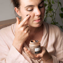 Load image into Gallery viewer, Woman applying face scrub to her face with a jar of scrub in her hand.
