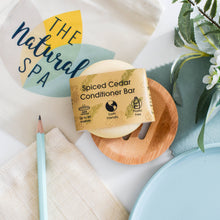 Load image into Gallery viewer, Spiced Cedar Conditioner Bar from The Natural Spa on a wooden plate with a plant and pencil in the background.
