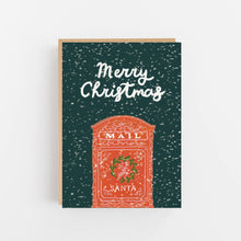 Load image into Gallery viewer, A Christmas greeting card with a dark teal background speckled with white snowflakes, featuring the words 'Merry Christmas' in white script and an illustration of a red Santa mail box. The card is shown standing upright with a kraft envelope behind it against a clean white background.
