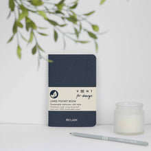Load image into Gallery viewer, Navy blue notebook with beige label on a white surface with a candle and plant in the background
