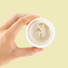 Load image into Gallery viewer, Hand holding a small jar of cream against a light yellow background
