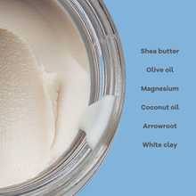 Load image into Gallery viewer, Close-up of a jar with cream inside, showing shea butter, olive oil, magnesium, coconut oil, arrowroot, and white clay on a blue background.

