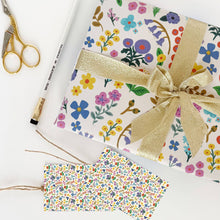 Load image into Gallery viewer, Floral-patterned gift wrap with a gold ribbon, scissors, and pen on a white background
