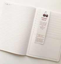 Load image into Gallery viewer, Open notebook with a cherry fruit-themed page marker on a white background
