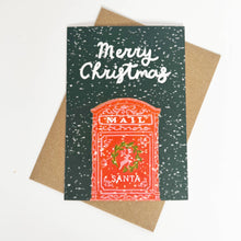 Load image into Gallery viewer, A Christmas greeting card with a dark green speckled background, white 'Merry Christmas' script, and a red-orange mailbox illustration featuring Santa and the words 'MAIL' and 'SANTA'. The card is layered over a brown kraft envelope on a white background.
